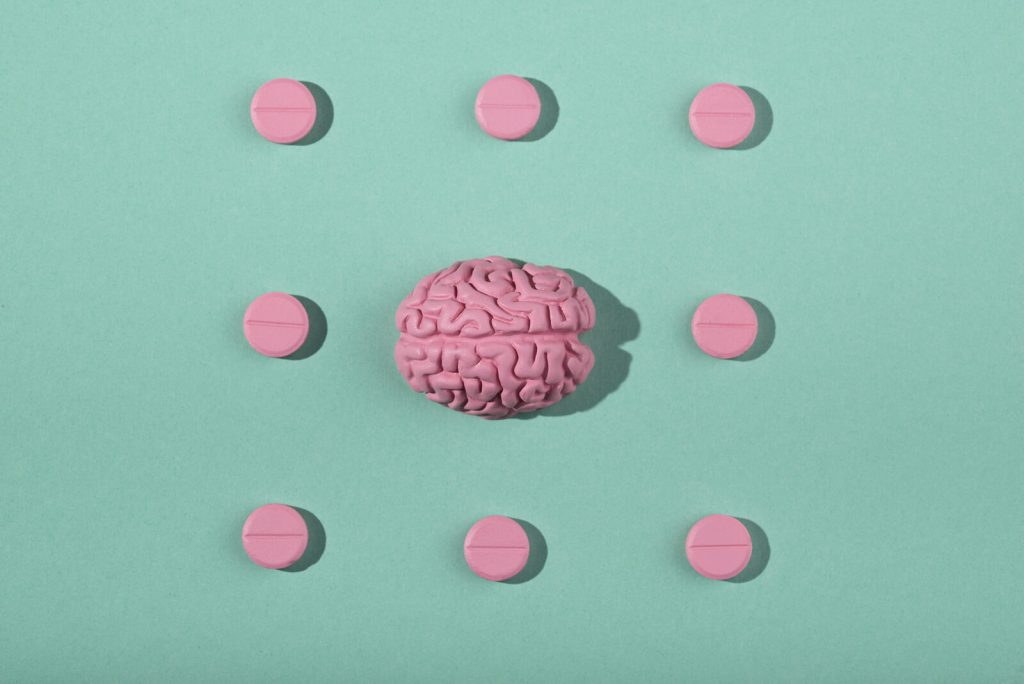 Cerebro rosa rodeado de pastillas rosas sobre fondo verde, metáfora de los neurotransmisores que potencian el rendimiento del opositor